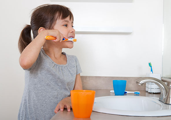 A young girl is brushing her teeth in the bathroom mirror