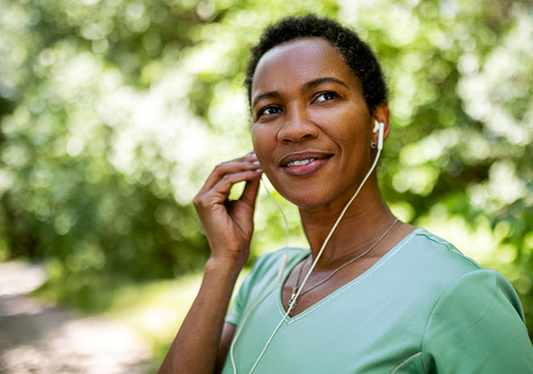 A woman is putting in her headphones before going on a run on a trail outside