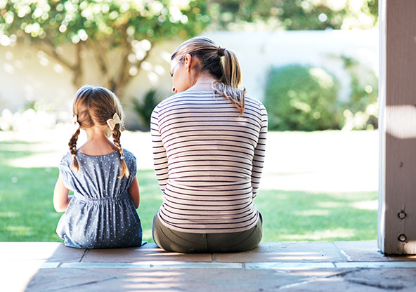 A young girl and her mom, sitting side-by-side on their back porch. 