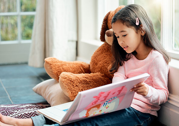Little girl reading to teddy bear