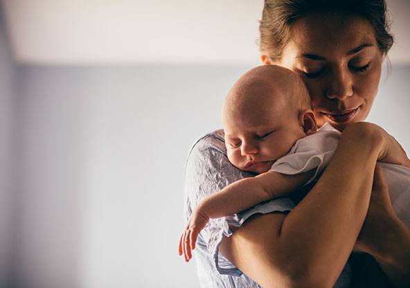 A mom is holding a sleeping newborn baby