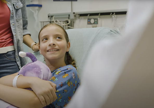 Little girl hugging a stuffed animal and smiling as she listens to the doctor explain her upcoming surgery.