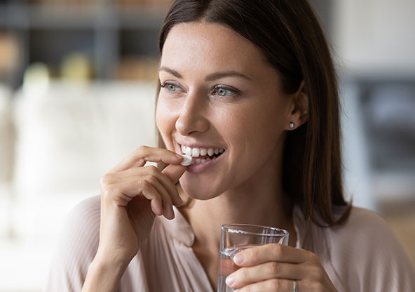 A young woman is holding a glass of water and taking a prenatal vitamin.