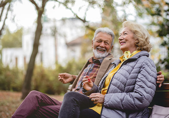 Happy, senior couple sitting on the bench in a park. Signs of throat cancer