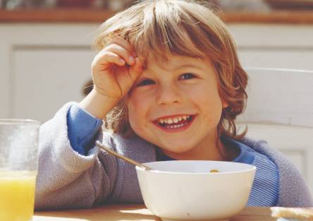 A young boy smiles over a breakfast of cereal and orange juice