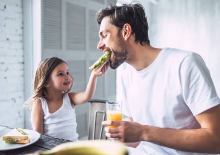 A dad takes a bite of a sandwich being held by his daughter