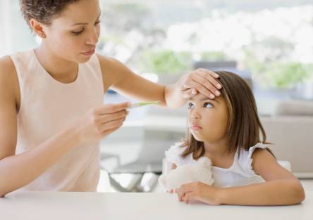 A mom puts her hand to her daughter's forehead as she looks at a thermometer