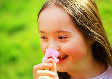 A smiling girl stops to smell a pink flower