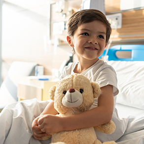 A little boy on a hospital bed smiling with his teddy bear