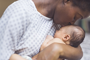 Black mom in a hospital gown kissing her newborn baby