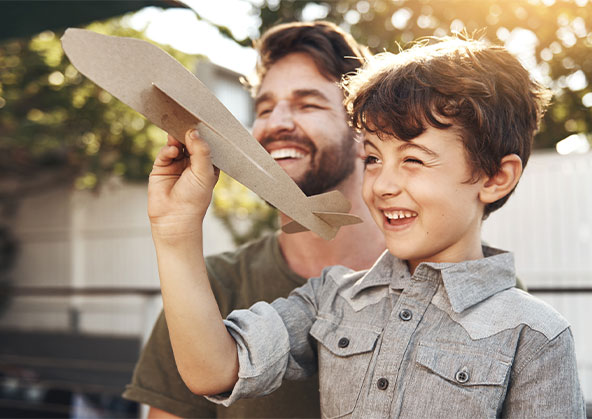 A young boy throwing his paper plane outside with his dad