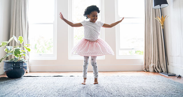 Happy girl performing ballet dance at home. Little girl is wearing tutu while practicing. She is dancing against windows.