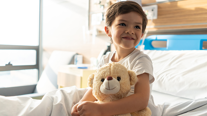 A little boy in the hospital bed with a teddy bear