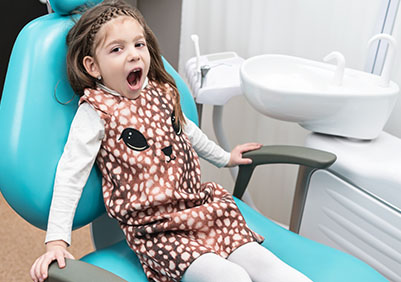 Little girl sitting in a dental chair with an open mouth.