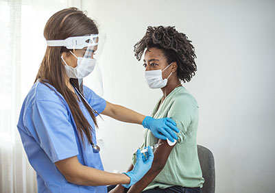Side view shot of female nurse wearing protective mask and gloves preparing medical syringe for giving injection to patient. 