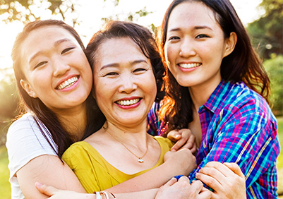 Asian mom and two daughters hugging outside