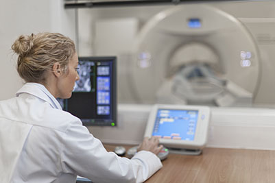A doctor is sitting in front of the computers and MRI machine