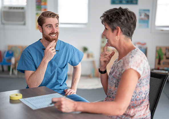 A speech therapist works with an adult woman patient on speech therapy
