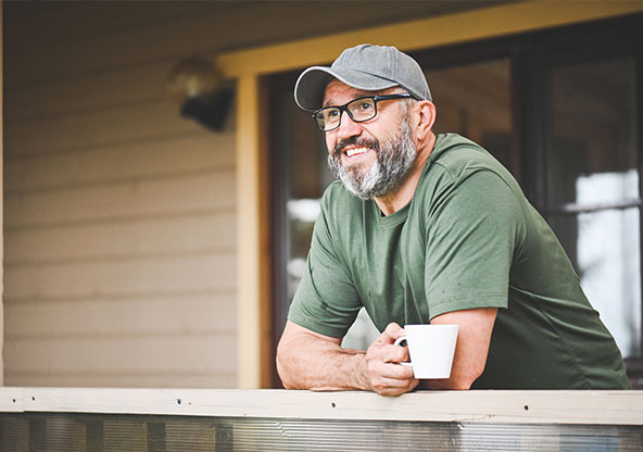 man smiling on his porch with coffee