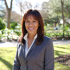 Hispanic woman in a suit with mid-length brunette hair smiling at the camera. 