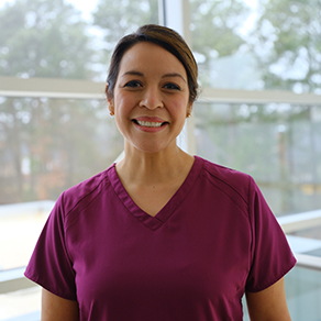 Happy CHRISTUS nurse smiling into the camera with maroon scrubs on